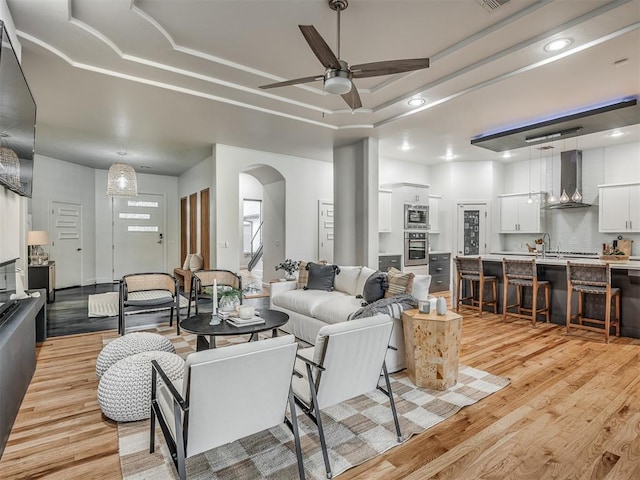 3604 Valley Creek Cir, Edmond, OK 73034 - living room featuring ceiling fan, light wood-style flooring, arched walkways, recessed lighting, and a tray ceiling