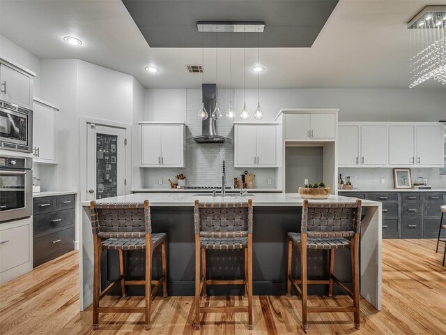 3604 Valley Creek Cir, Edmond, OK 73034 - kitchen featuring wall chimney exhaust hood, stainless steel appliances, light wood-style floors, white cabinets, and light countertops