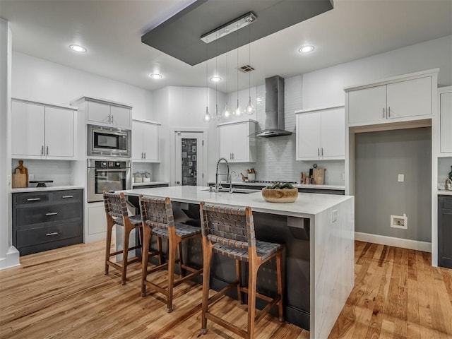 3604 Valley Creek Cir, Edmond, OK 73034 - kitchen featuring appliances with stainless steel finishes, wall chimney exhaust hood, a breakfast bar, light countertops, and a center island with sink