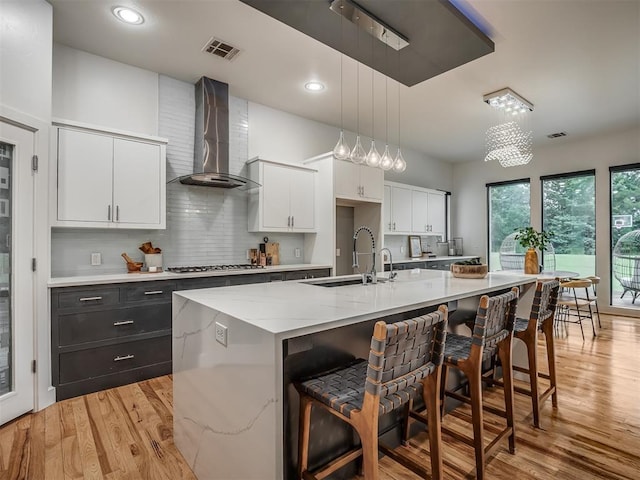 3604 Valley Creek Cir, Edmond, OK 73034 - kitchen with wall chimney range hood, white cabinetry, light wood-style flooring, a breakfast bar area, and recessed lighting