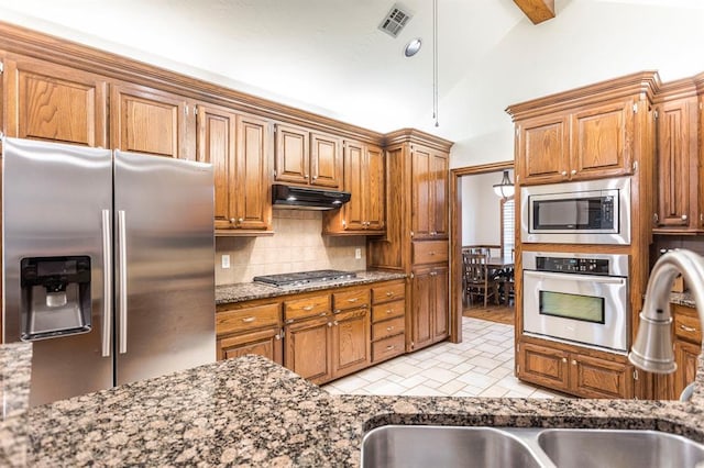 2525 Steeplechase Rd, Edmond, OK 73034 - kitchen featuring appliances with stainless steel finishes, tasteful backsplash, under cabinet range hood, dark stone counters, and brown cabinetry