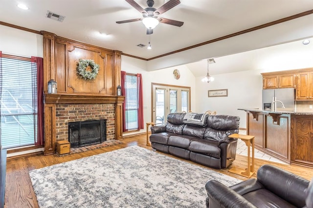 2525 Steeplechase Rd, Edmond, OK 73034 - living room featuring a ceiling fan, light wood finished floors, ornamental molding, a brick fireplace, and vaulted ceiling