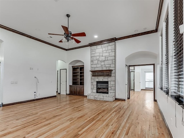 18501 El Greco Dr, Edmond, OK 73012 - unfurnished living room featuring ceiling fan, crown molding, a fireplace, light wood-style floors, and arched walkways