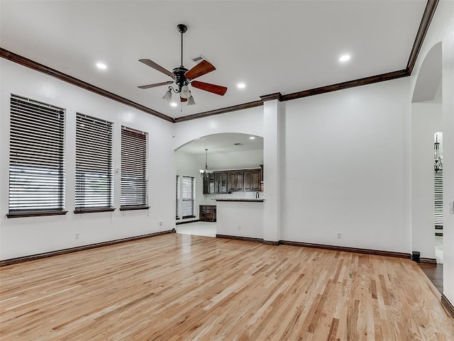18501 El Greco Dr, Edmond, OK 73012 - unfurnished living room with arched walkways, crown molding, a ceiling fan, a chandelier, and light wood-style flooring