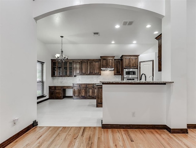18501 El Greco Dr, Edmond, OK 73012 - kitchen with stainless steel microwave, arched walkways, dark brown cabinets, light wood-style flooring, and under cabinet range hood