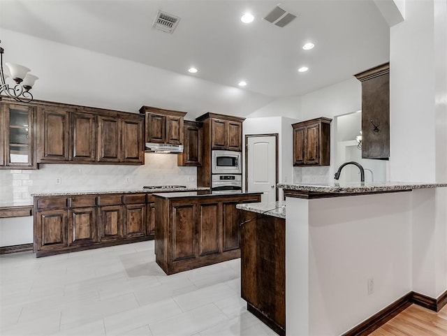 18501 El Greco Dr, Edmond, OK 73012 - kitchen with stainless steel appliances, under cabinet range hood, decorative backsplash, dark brown cabinets, and vaulted ceiling