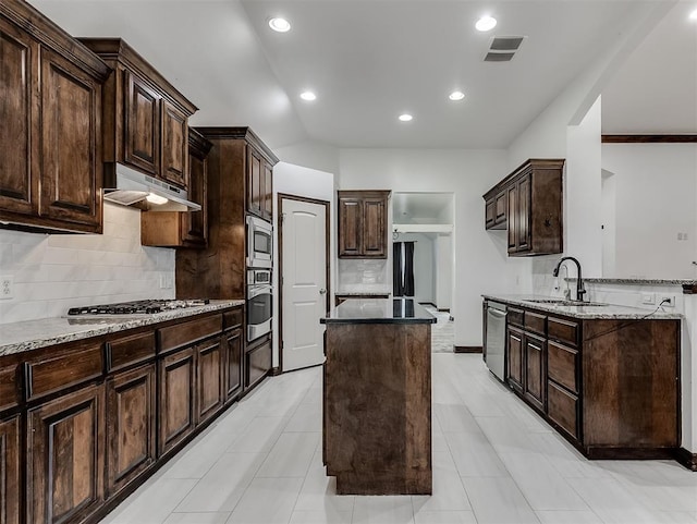18501 El Greco Dr, Edmond, OK 73012 - kitchen with under cabinet range hood, stainless steel appliances, decorative backsplash, dark brown cabinetry, and light stone counters