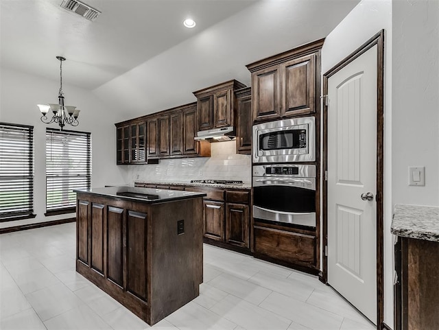 18501 El Greco Dr, Edmond, OK 73012 - kitchen with stainless steel appliances, under cabinet range hood, vaulted ceiling, tasteful backsplash, and a chandelier