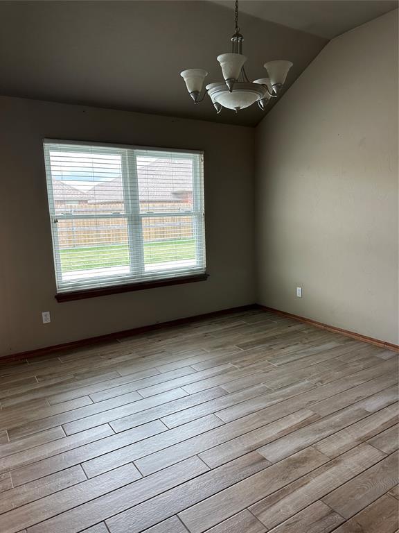 712 N Cherokee Way, Mustang, OK 73064 - empty room featuring a chandelier, healthy amount of natural light, light wood-style floors, and vaulted ceiling
