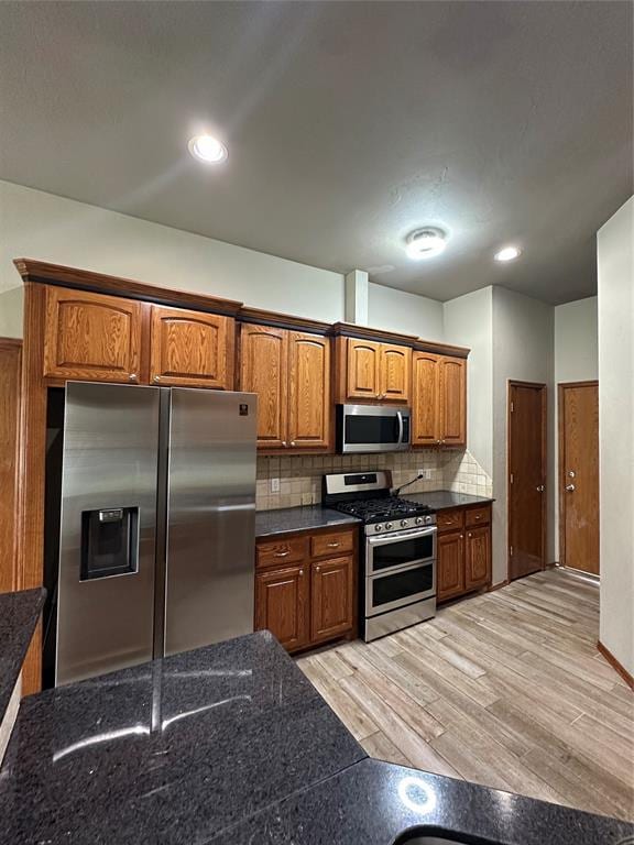 712 N Cherokee Way, Mustang, OK 73064 - kitchen with appliances with stainless steel finishes, brown cabinetry, backsplash, light wood-style floors, and dark stone counters