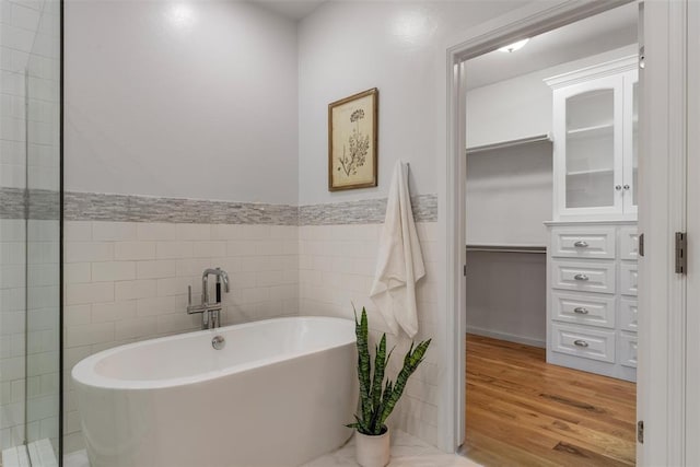 1517 Station St, Edmond, OK 73034 - bathroom with tile walls, a soaking tub, wood finished floors, and a walk in closet