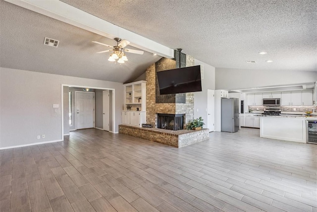 1909 Magnolia Ln, Edmond, OK 73013 - unfurnished living room with a textured ceiling, ceiling fan, wine cooler, beam ceiling, and a large fireplace