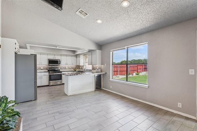 1909 Magnolia Ln, Edmond, OK 73013 - kitchen with appliances with stainless steel finishes, beverage cooler, a textured ceiling, white cabinets, and a peninsula