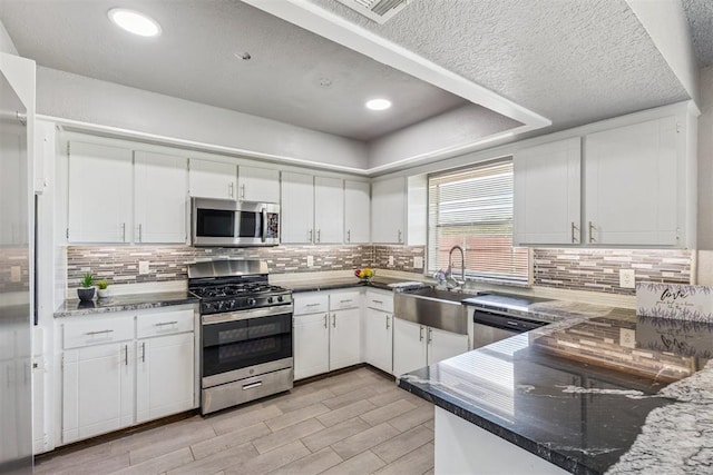 1909 Magnolia Ln, Edmond, OK 73013 - kitchen featuring appliances with stainless steel finishes, light wood finished floors, white cabinetry, decorative backsplash, and a textured ceiling