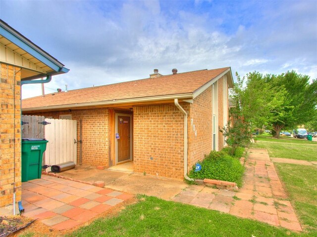 704 NW 137th St, Edmond, OK 73013 - view of exterior entry with brick siding, a yard, a patio area, roof with shingles, and a chimney