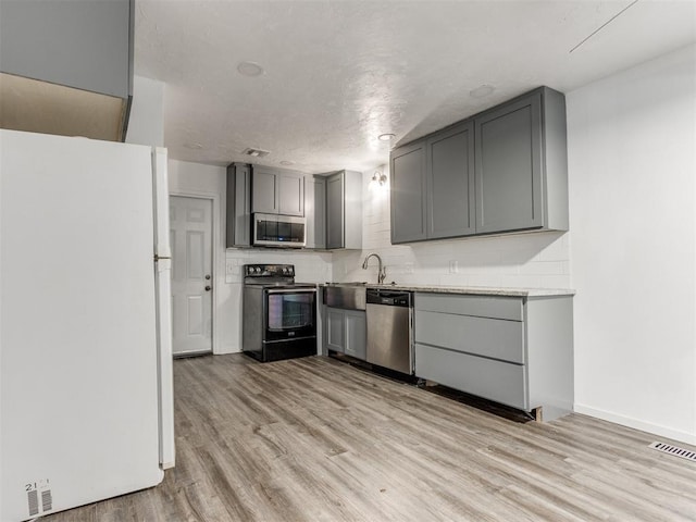 704 NW 137th St, Edmond, OK 73013 - kitchen with appliances with stainless steel finishes, gray cabinetry, backsplash, and light wood-style flooring