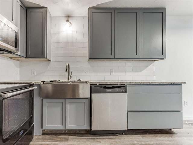 704 NW 137th St, Edmond, OK 73013 - kitchen with appliances with stainless steel finishes, gray cabinetry, light wood-type flooring, decorative backsplash, and light stone countertops