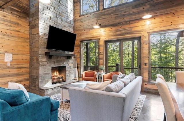 2105 Pine Hills Rd, Broken Bow, OK 74728 - living room featuring wooden walls, a stone fireplace, a high ceiling, and finished concrete floors