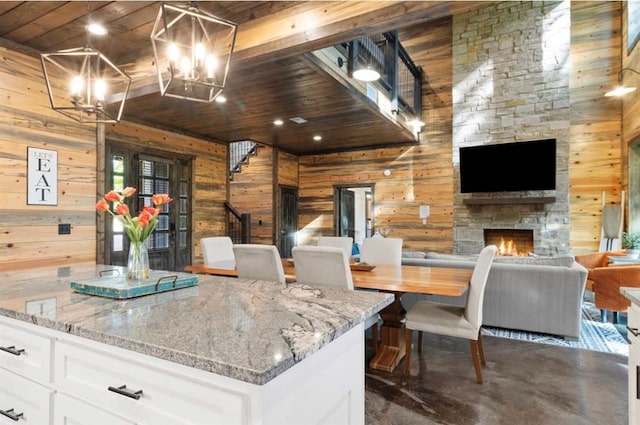 2105 Pine Hills Rd, Broken Bow, OK 74728 - kitchen with open floor plan, wood walls, a chandelier, white cabinetry, and a fireplace