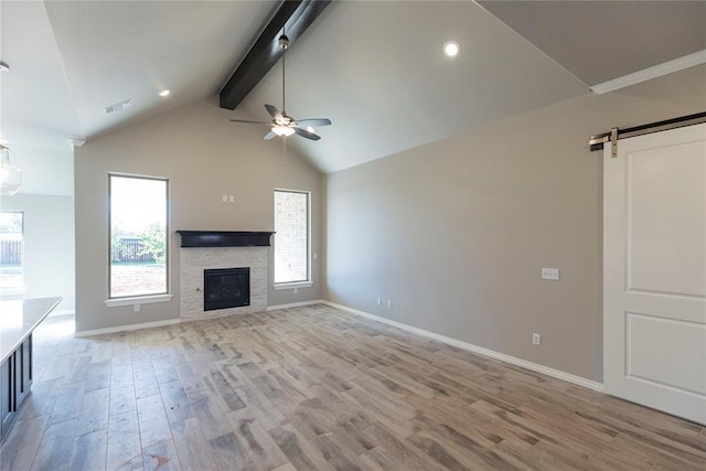 1624 NE 32nd St, Moore, OK 73160 - unfurnished living room with beamed ceiling, a barn door, light wood finished floors, ceiling fan, and a stone fireplace