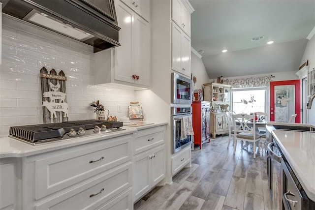 1624 NE 32nd St, Moore, OK 73160 - kitchen with stainless steel appliances, extractor fan, vaulted ceiling, white cabinets, and decorative backsplash