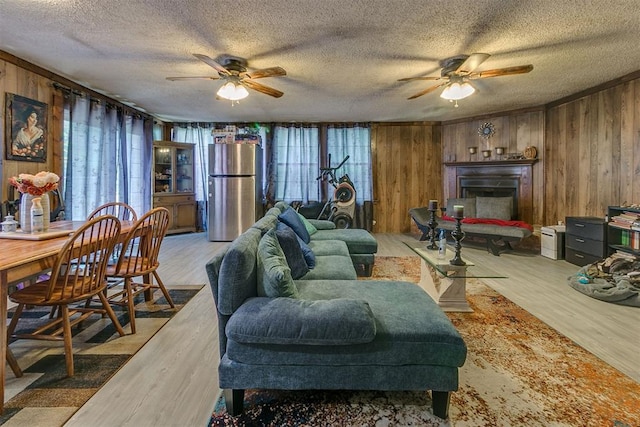 2317 N Redmond Ave, Bethany, OK 73008 - living area featuring ceiling fan, wooden walls, a textured ceiling, wood finished floors, and a fireplace with raised hearth
