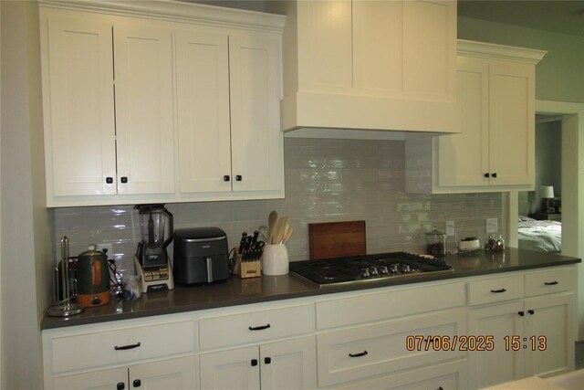 3909 Sorano Dr, Moore, OK 73160 - kitchen with stainless steel gas stovetop, dark countertops, decorative backsplash, and white cabinets