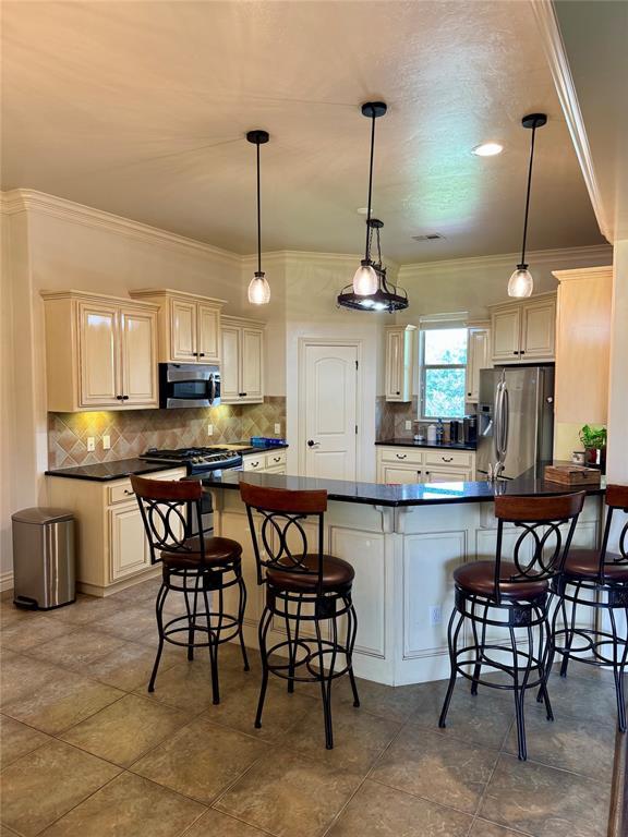 2803 Hidden Prairie Way, Edmond, OK 73013 - kitchen with stainless steel appliances, dark countertops, ornamental molding, and a breakfast bar area