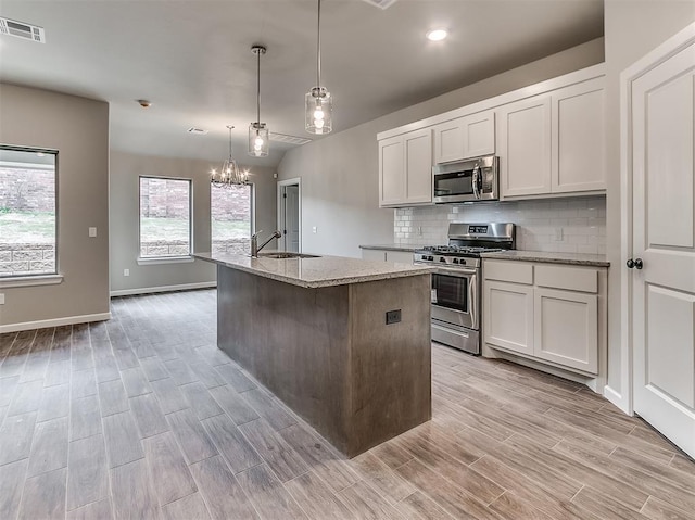600 Mirano Ln, Edmond, OK 73034 - kitchen featuring stainless steel appliances, a chandelier, a center island with sink, light wood-style flooring, and light stone countertops