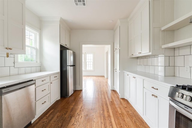 826 NE 18th St, Oklahoma City, OK 73105 - kitchen featuring appliances with stainless steel finishes, decorative backsplash, light wood-style floors, white cabinetry, and light countertops