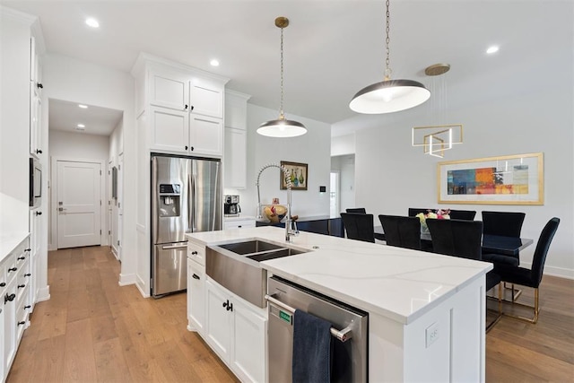 209 Pont Neuf Ct, Edmond, OK 73034 - kitchen featuring appliances with stainless steel finishes, light wood-style flooring, an island with sink, white cabinets, and hanging light fixtures