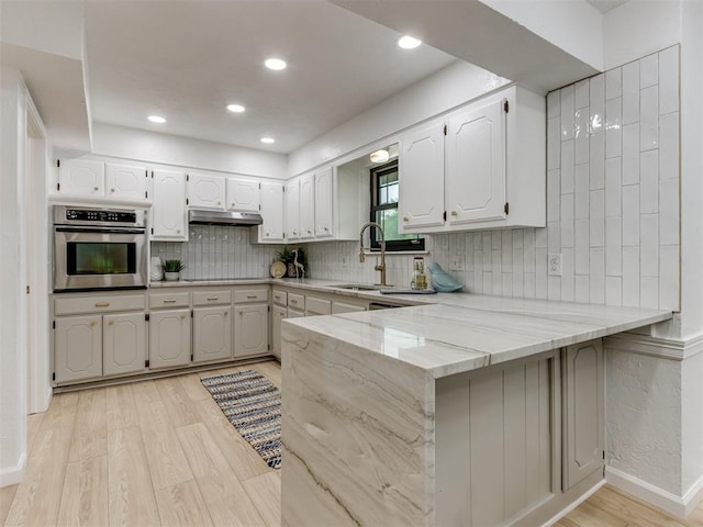 5412 Cloverlawn Dr, Oklahoma City, OK 73135 - kitchen featuring stainless steel oven, light wood-style floors, under cabinet range hood, a peninsula, and tasteful backsplash