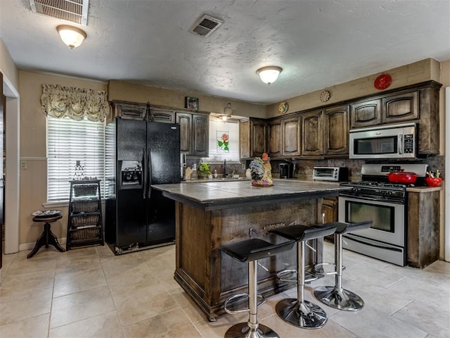 1200 Kingston Dr, Yukon, OK 73099 - kitchen featuring appliances with stainless steel finishes, a kitchen island, a breakfast bar area, dark brown cabinetry, and a textured ceiling