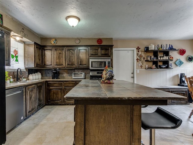 1200 Kingston Dr, Yukon, OK 73099 - kitchen featuring stainless steel appliances, dark brown cabinets, a center island, a breakfast bar area, and a textured ceiling
