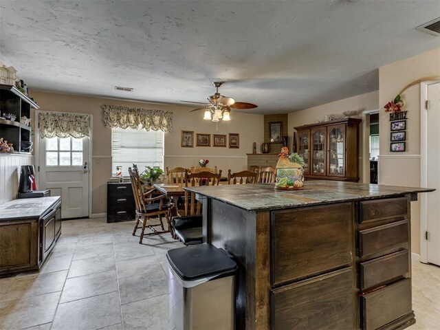 1200 Kingston Dr, Yukon, OK 73099 - kitchen with ceiling fan, dark brown cabinetry, open shelves, a center island, and light tile patterned floors