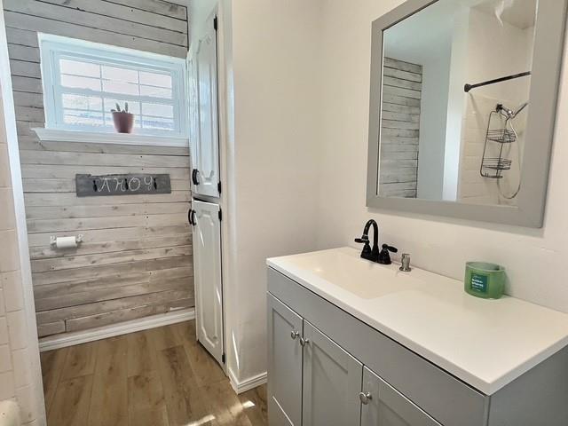 1024 E 12th St, Cushing, OK 74023 - bathroom featuring wood finished floors, vanity, wooden walls, and a shower