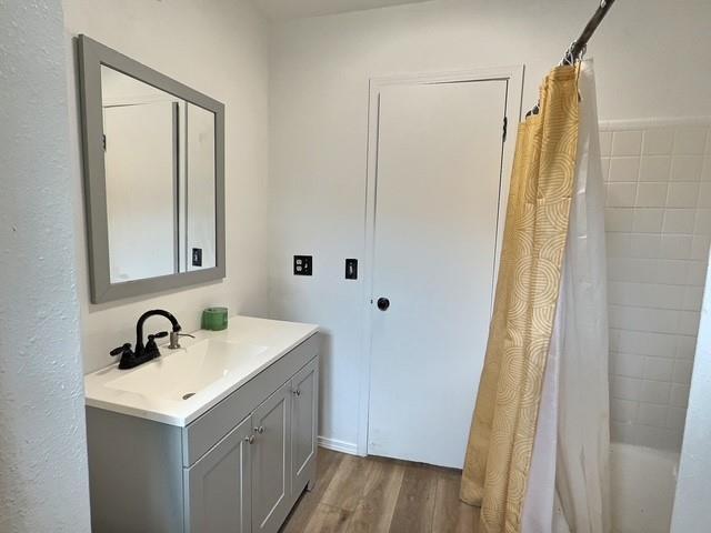 1024 E 12th St, Cushing, OK 74023 - bathroom with wood finished floors, vanity, and shower / bathtub combination with curtain