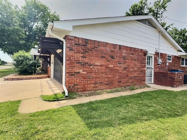 1024 E 12th St, Cushing, OK 74023 - view of property exterior featuring a garage, brick siding, and a yard