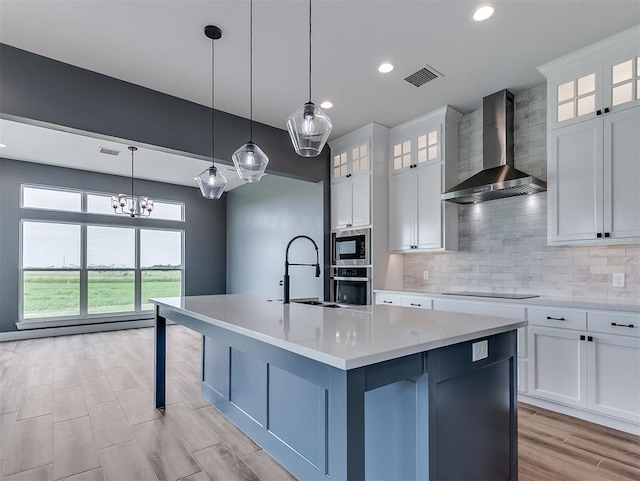 7431 NE Hawk Dr, Piedmont, OK 73078 - kitchen featuring wall chimney exhaust hood, appliances with stainless steel finishes, light countertops, an island with sink, and backsplash