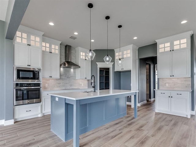 7431 NE Hawk Dr, Piedmont, OK 73078 - kitchen featuring stainless steel appliances, wall chimney exhaust hood, tasteful backsplash, light wood-type flooring, and light countertops