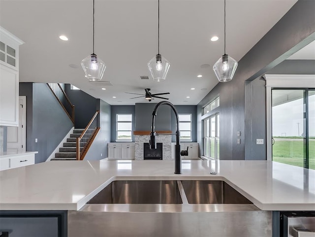7431 NE Hawk Dr, Piedmont, OK 73078 - kitchen featuring open floor plan, light countertops, a stone fireplace, ceiling fan, and white cabinetry