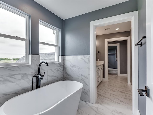 7431 NE Hawk Dr, Piedmont, OK 73078 - bathroom featuring marble finish flooring, a soaking tub, vanity, a wainscoted wall, and tile walls