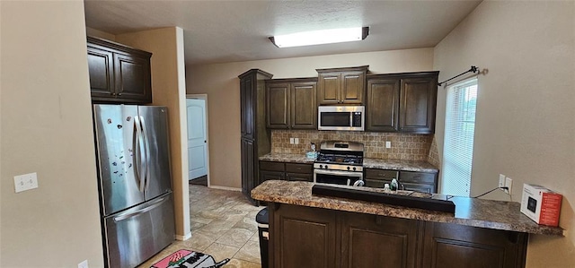12201 Buckingham Ln, Yukon, OK 73099 - kitchen featuring appliances with stainless steel finishes, dark brown cabinets, decorative backsplash, a peninsula, and dark countertops