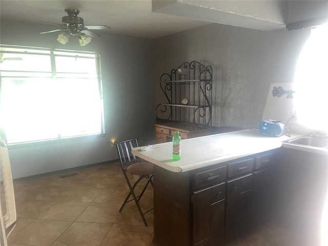 kitchen with light tile patterned floors, a ceiling fan, a breakfast bar, a peninsula, and dark brown cabinets
