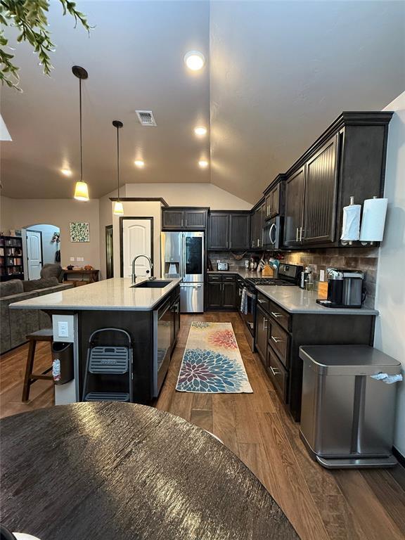 18641 Como Dr, Edmond, OK 73012 - kitchen featuring appliances with stainless steel finishes, open floor plan, an island with sink, light countertops, and lofted ceiling
