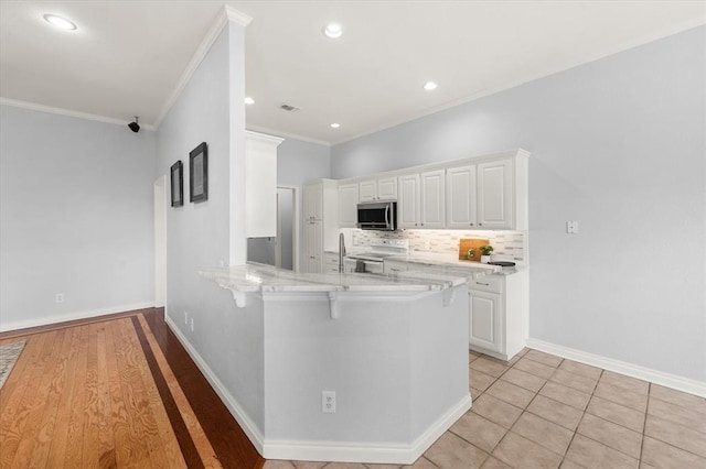 541 SW 154th Ct, Oklahoma City, OK 73170 - kitchen with stainless steel microwave, white range with electric stovetop, a kitchen bar, white cabinets, and crown molding