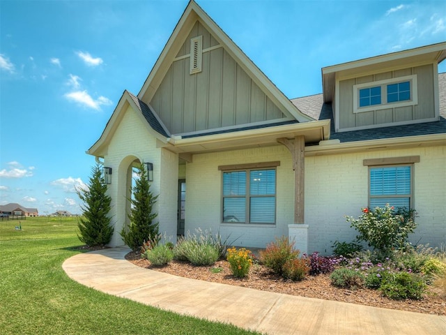 7290 NE Hawk Dr, Piedmont, OK 73078 - view of front of property with board and batten siding, brick siding, roof with shingles, and a front yard