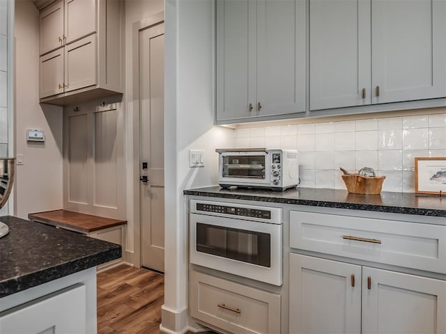7290 NE Hawk Dr, Piedmont, OK 73078 - kitchen featuring wood finished floors, tasteful backsplash, stainless steel oven, and dark stone countertops