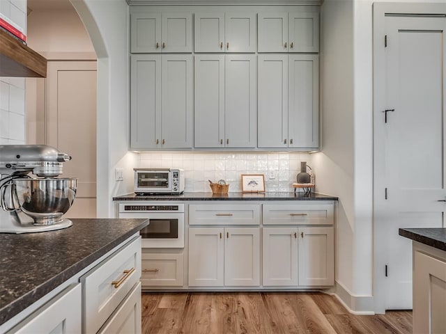 7290 NE Hawk Dr, Piedmont, OK 73078 - kitchen featuring arched walkways, tasteful backsplash, light wood-style floors, and dark stone countertops