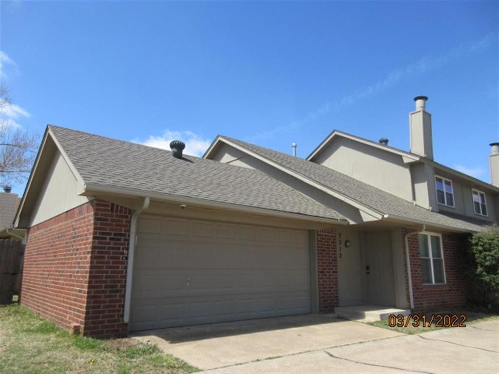 7312 NW 94th St, Oklahoma City, OK 73162 - view of front of house with brick siding, a garage, driveway, a chimney, and a shingled roof